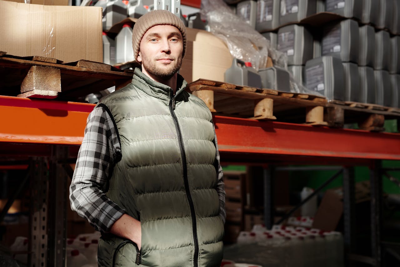 A man in a green vest stands confidently in a warehouse, illuminated by natural light.